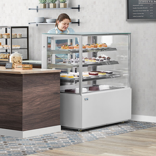 A woman looking at cakes in a refrigerated bakery display case.