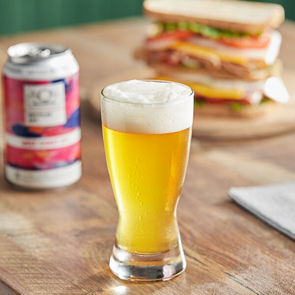 A glass of Untitled Art West Coast IPA with foam next to a can of beer on a wooden table.