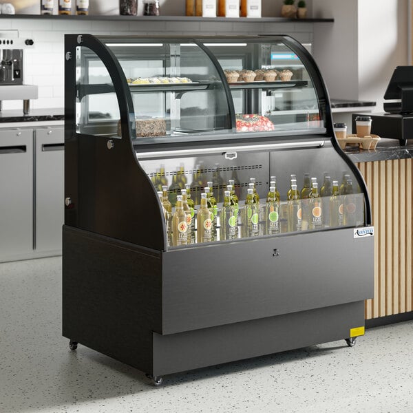 An Avantco black curved refrigerated air curtain merchandiser on a counter with bottles of liquid in it.