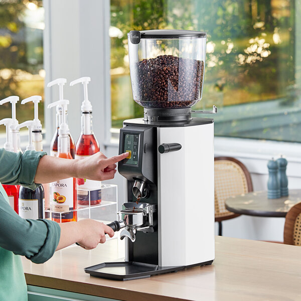 A woman using a white Anfim espresso grinder on a counter.