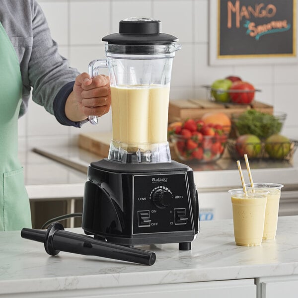 A person using a Galaxy commercial blender to make a yellow smoothie.