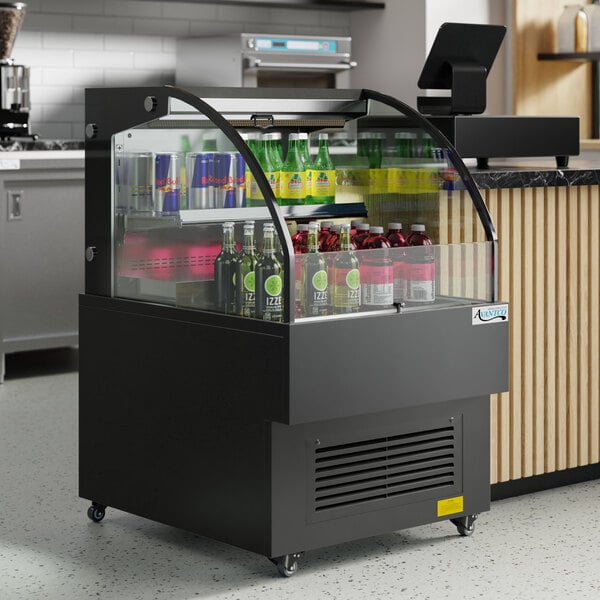 An Avantco black horizontal air curtain beverage cooler with drinks on a shelf.
