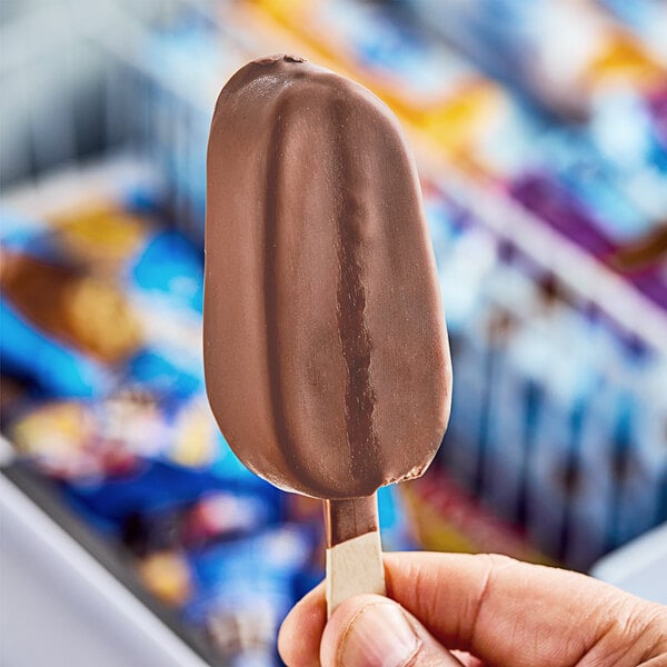 A person's hand holding a chocolate Oatly ice cream bar.