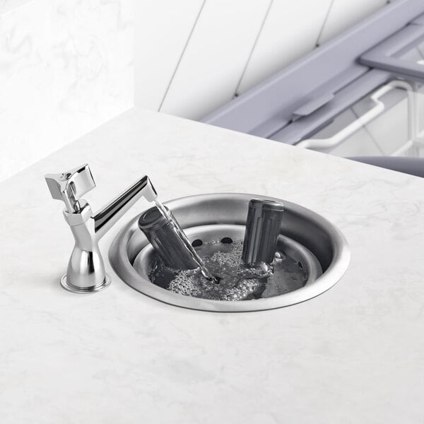 A Regency stainless steel dipper well bowl in a sink with water running from a faucet.