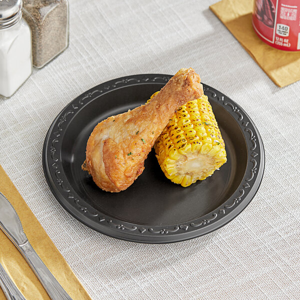 A plate of fried chicken and corn on the cob on a Ecopax black polypropylene plate.