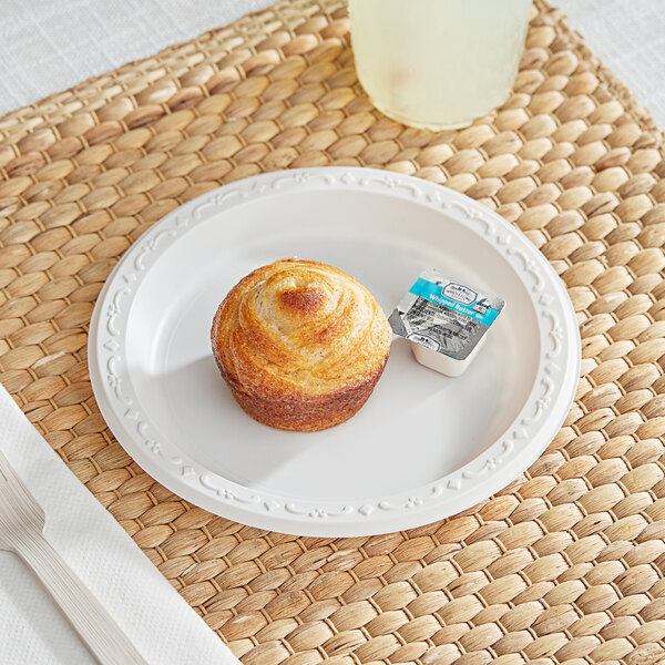 A white Ecopax polypropylene plate with a muffin on it on a table with a glass of water.