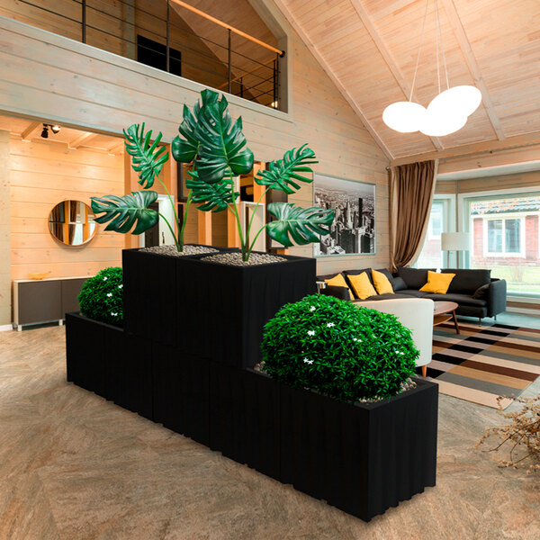 A white Floridis square planter with a green bush next to a couch.