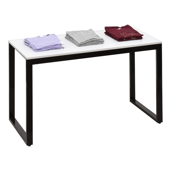 A rectangular display table with a white top and black legs holding folded shirts.