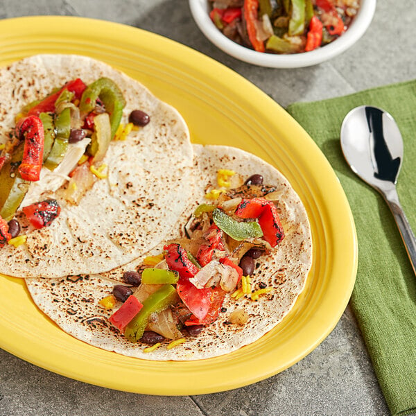 A yellow plate with two tortillas filled with Sevillo Fire Grilled Onion and Peppers next to a bowl of the vegetables.