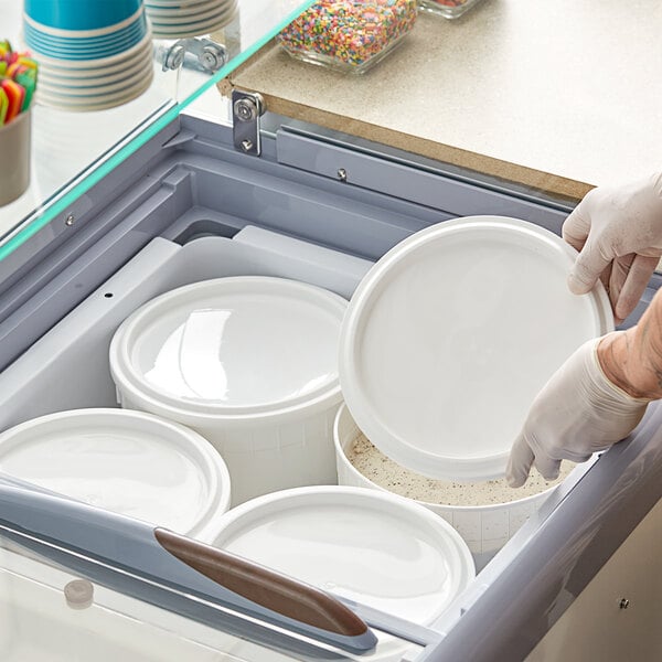 A person wearing gloves holding a White LDPE Ice Cream Tub Cover.