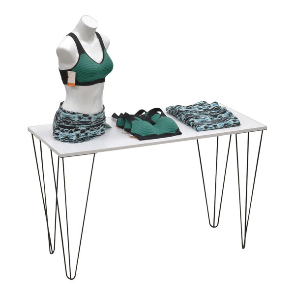 A white rectangular display table with a black and blue patterned cloth and a mannequin wearing a green and black sports garment.