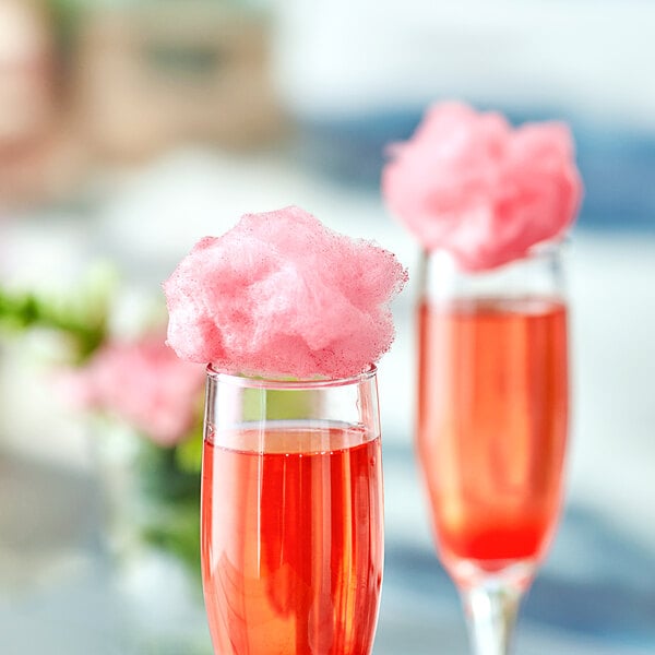 Two glasses of red liquid with pink cotton candy on top.