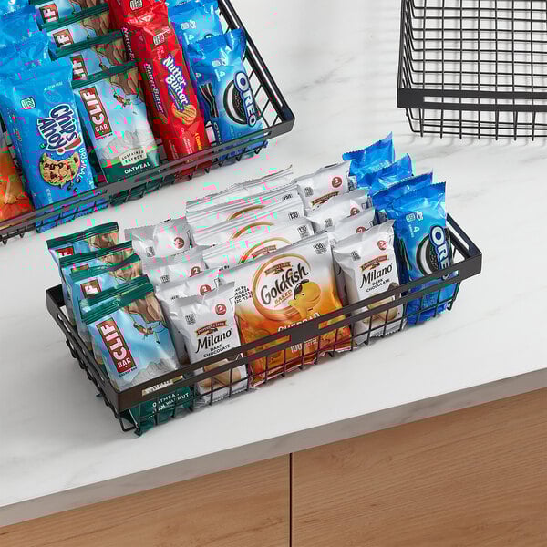 An American Metalcraft black metal display basket filled with bags of chips on a hotel counter.