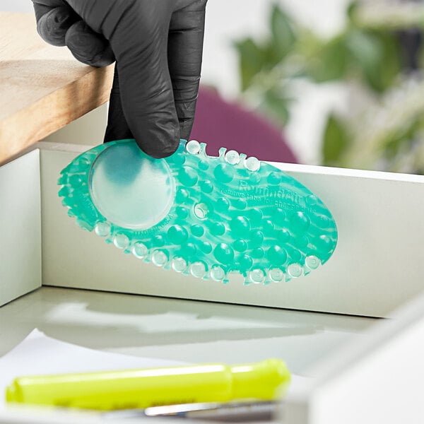 A close-up of a rubber gloved hand holding a Fresh Products Curve Cucumber Melon passive air freshener pad.