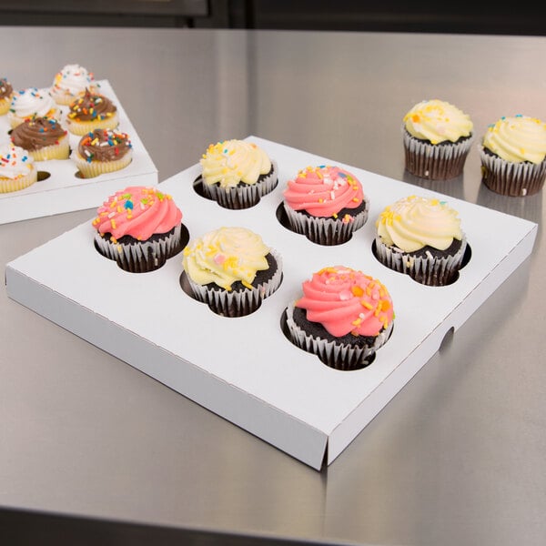 A group of cupcakes in a Baker's Lane white box with a reversible cupcake insert. Each cupcake has yellow or pink frosting with sprinkles.