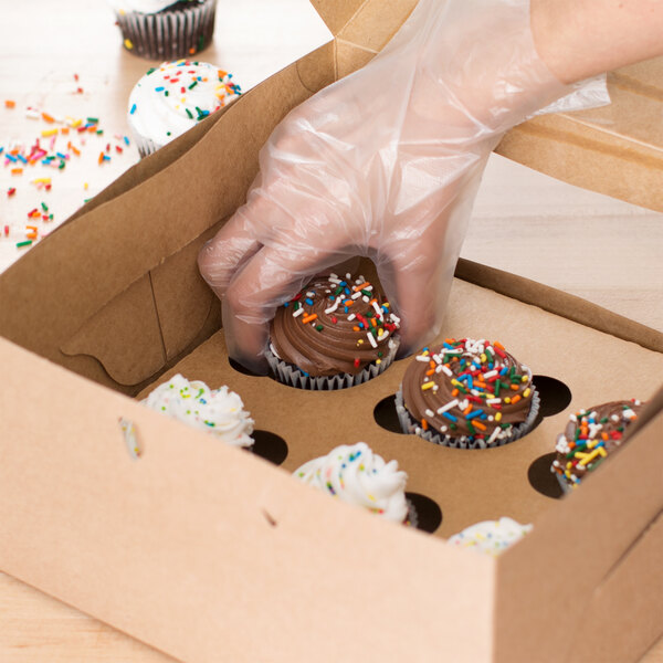 A person putting a chocolate frosted cupcake with sprinkles in a Baker's Lane cupcake box.