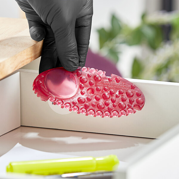 A hand in a black glove holding a red Fresh Products Curve air freshener.