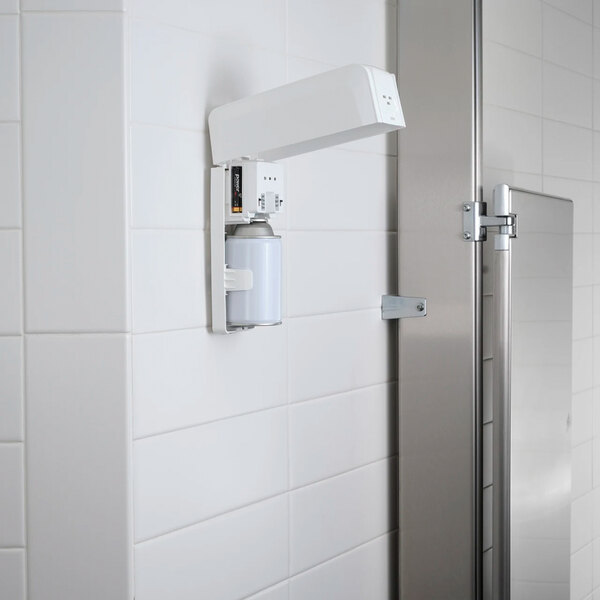 A white metered aerosol air freshener cabinet mounted on a tiled wall.