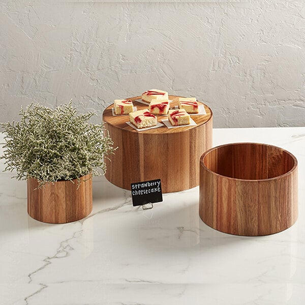 An American Metalcraft acacia wood riser set with wooden containers holding a plant and desserts on a table.