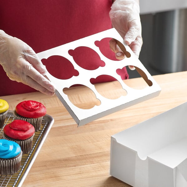 A person holding a white Baker's Lane cupcake box with a cupcake inside.