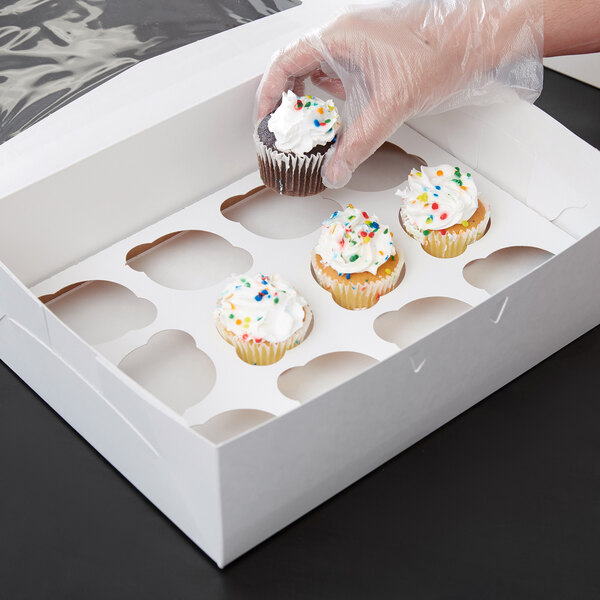 A hand holding a cupcake in a Baker's Lane white box with a clear window.