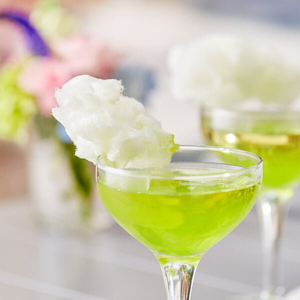 A close-up of a glass of green liquid with cotton candy on top.