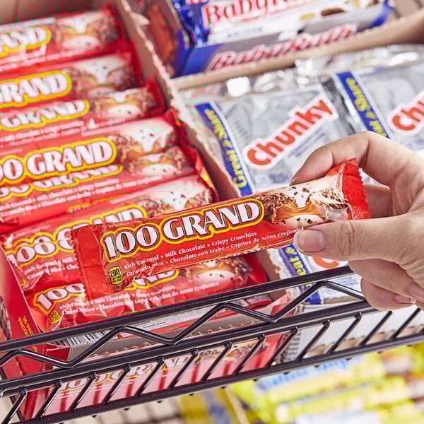 A hand holding a 100 GRAND Full Size Chocolate Bar.