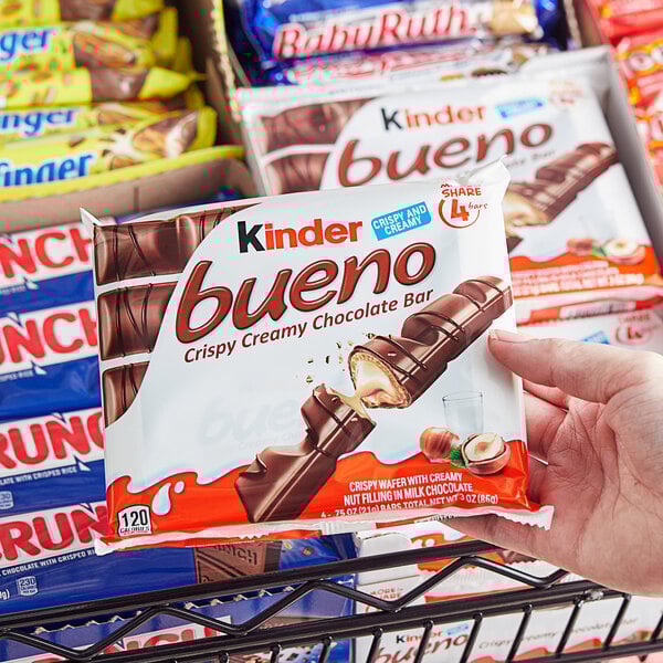 A hand holding a package of KINDER Bueno chocolate bars with a bite taken out of one.