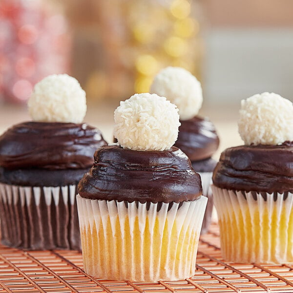 A close up of a chocolate cupcake with a white and chocolate frosting and a Raffaello candy on top.