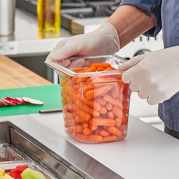 A person in gloves holding a Vollrath clear polycarbonate food pan of baby carrots.