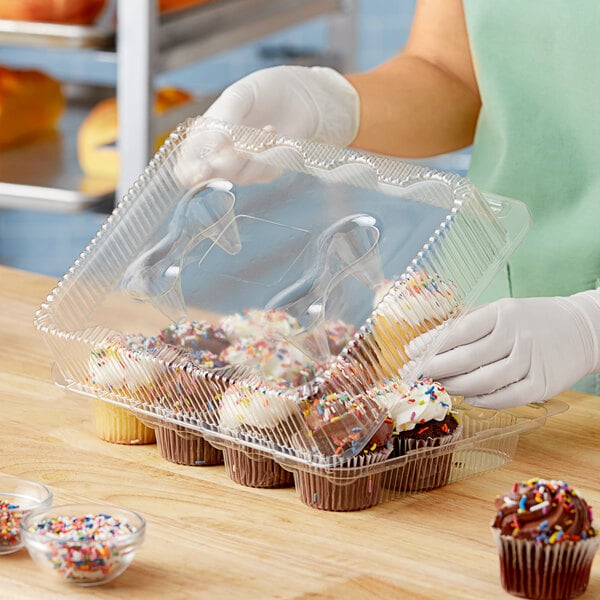 A woman in gloves putting a frosted cupcake with sprinkles in a clear plastic container with 12 compartments.