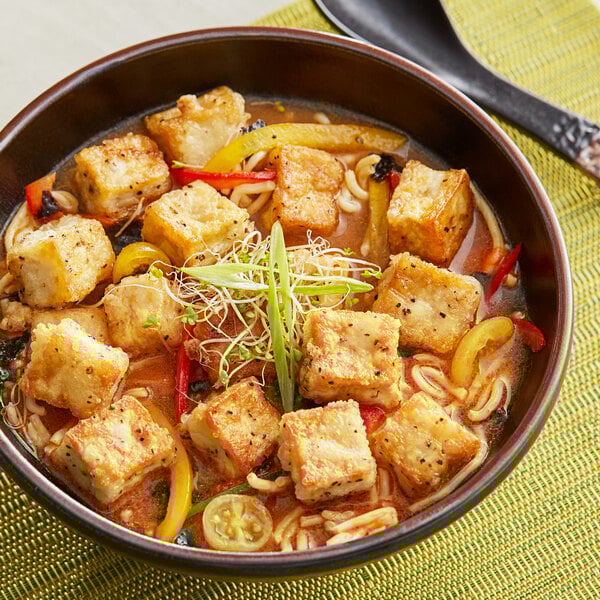 A bowl of soup with tofu and vegetables.