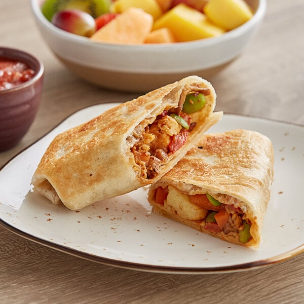 A JUST Egg Plant-Based Vegan Chili Crisp Breakfast Burrito on a plate with a bowl of fruit.