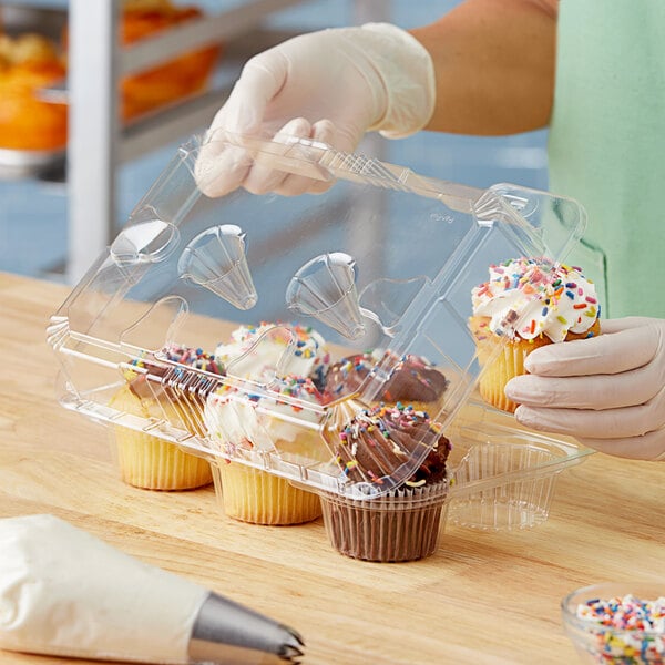 A person holding a cupcake in a Polar Pak plastic container with a yellow handle and clear lid.