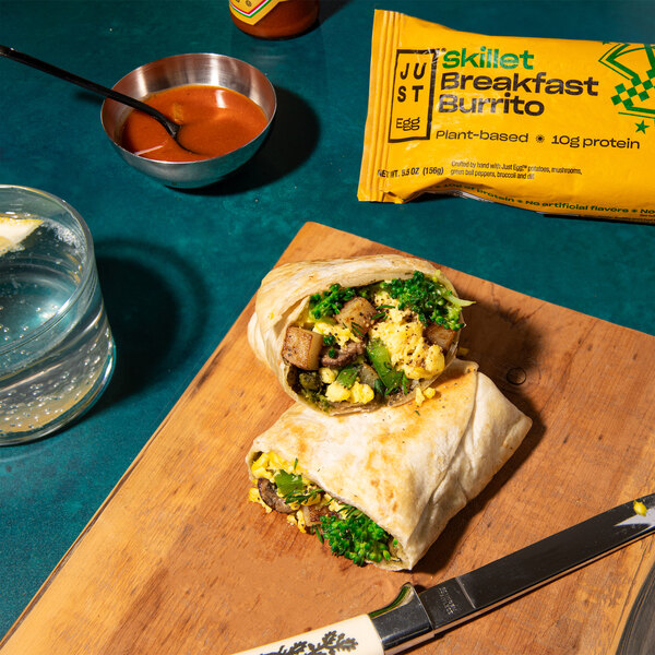 A cutting board with a Eat Just Egg vegan breakfast burrito and a bowl of sauce.