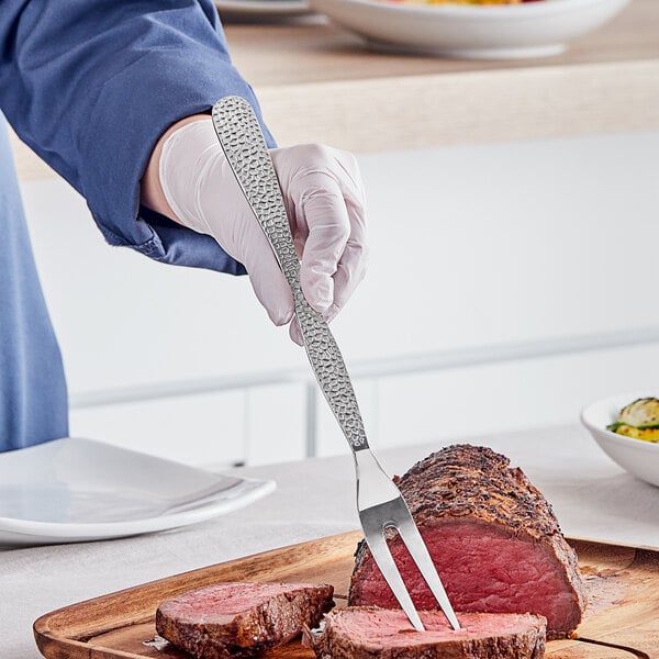 A person using an American Metalcraft stainless steel meat fork and knife to cut meat.