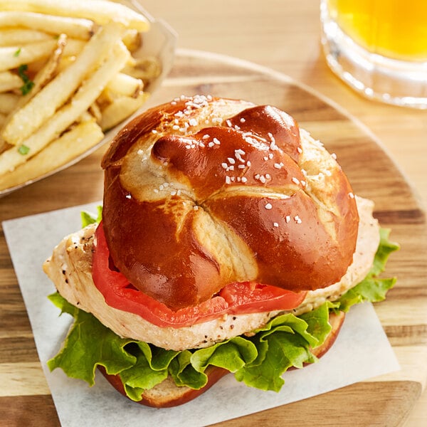 A sandwich on a Ditsch soft pretzel bun with fries on a wooden plate.