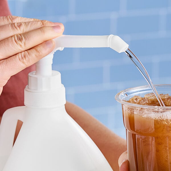 A person using a Lavex white plastic pump to dispense liquid into a clear cup.