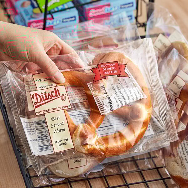 A hand holding a plastic bag of Ditsch soft pretzels