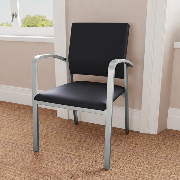 A Lesro Newport Patriot Plus black vinyl guest arm chair with silver legs in a room.