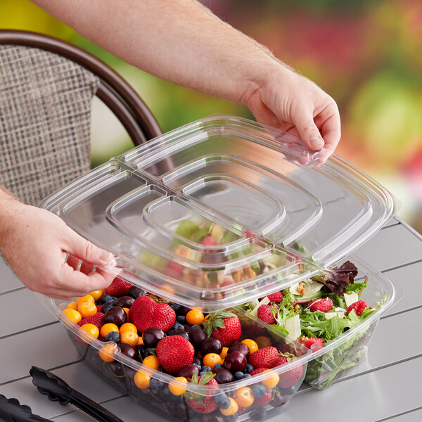 A person holding a plastic container with a Sabert clear pop-top lid full of fruit.