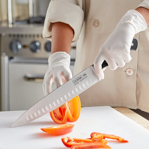 A person in white gloves using a Choice Classic Granton Edge Chef Knife to slice a tomato.