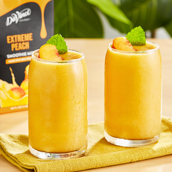 Two glasses of yellow DaVinci Gourmet peach smoothie with fruit on top.