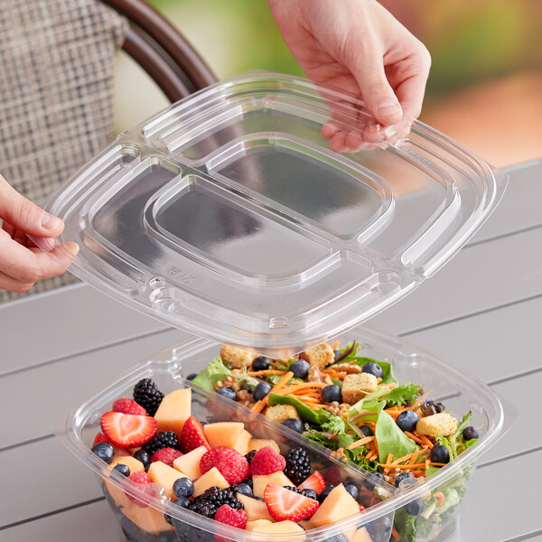 A hand opening a Sabert clear plastic container with salad inside.