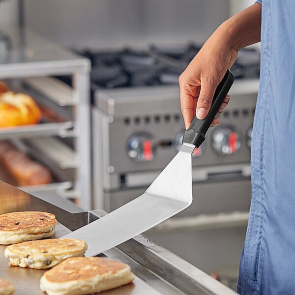 A hand using an American Metalcraft solid turner to lift a pancake off a griddle.