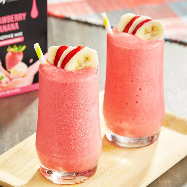 Two glasses of pink smoothies with straws and banana slices next to DaVinci Gourmet Strawberry Banana Smoothie Mix.