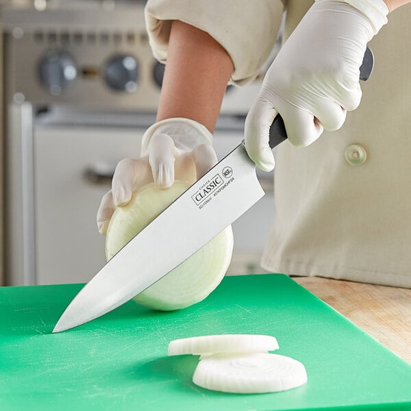 A person in gloves using a Choice Classic Short Bolster Chef Knife to slice an onion on a green cutting board.