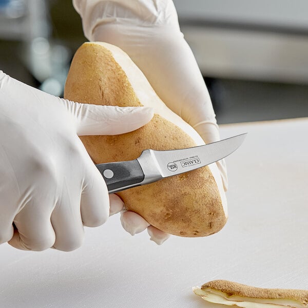 A person in gloves using a Choice Classic Bird's Beak Paring Knife to peel a potato.