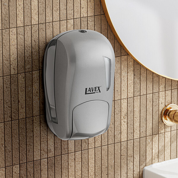 A Lavex Pro titanium manual liquid soap dispenser on a white wall above a brown countertop.
