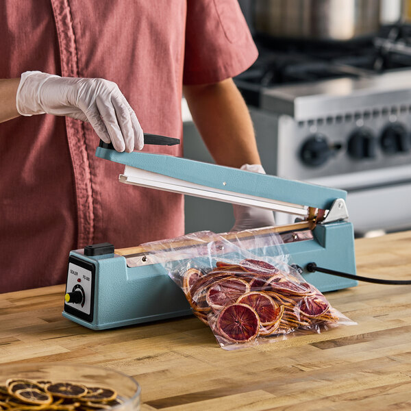 A Galaxy 12-inch impulse heat bag sealer with a timer being used to seal a plastic bag filled with dried citrus slices.